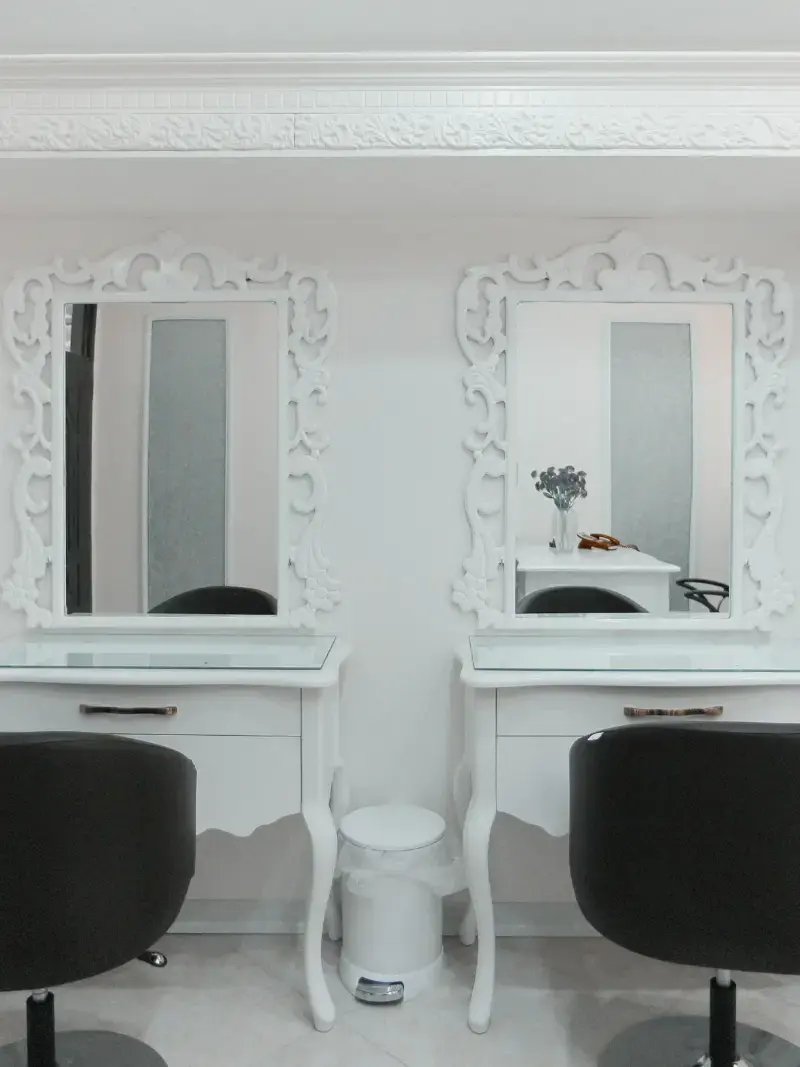 Two white vanity stations with tall mirrors in a bright salon