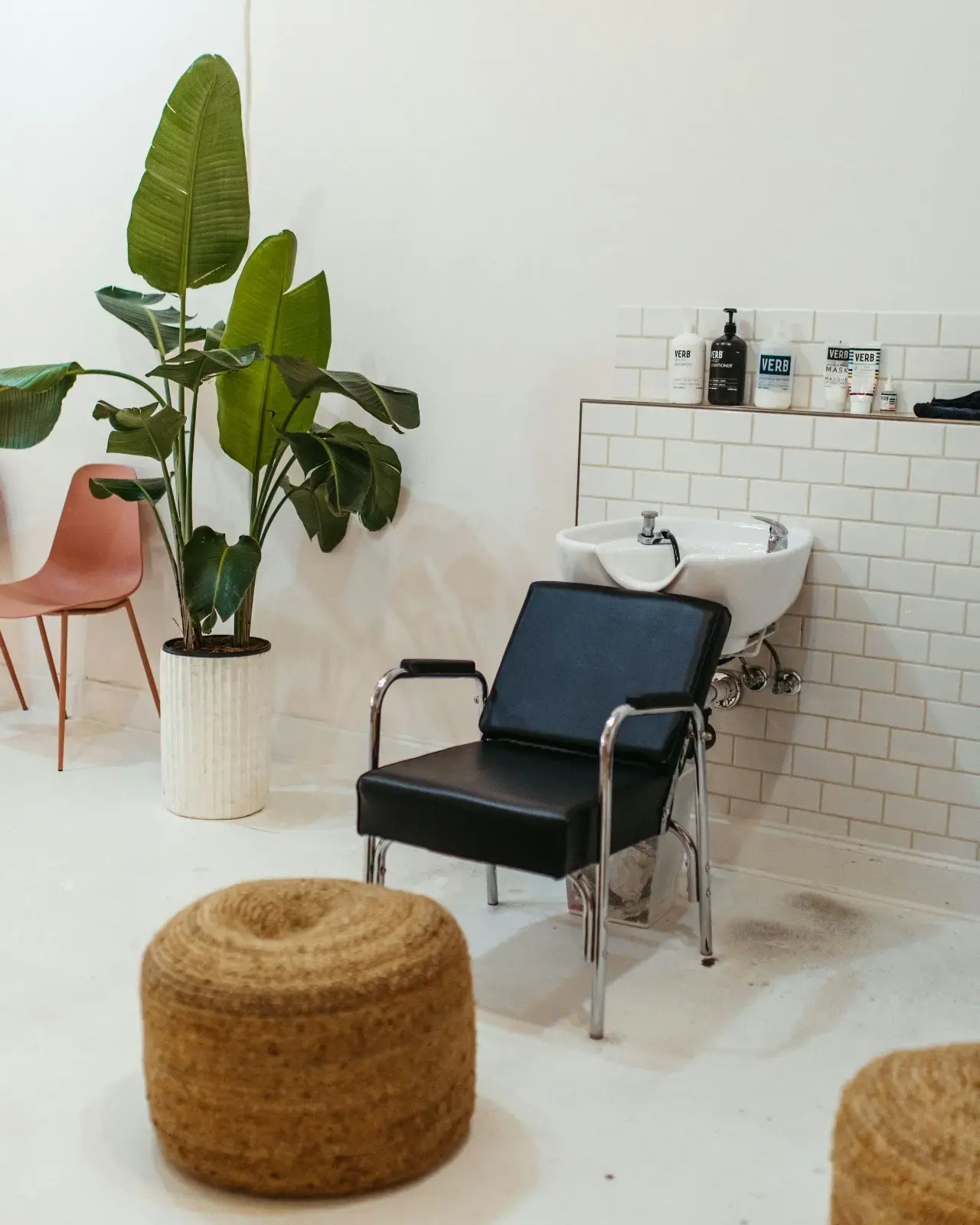 A bright white-tiled salon room with a styling chair, basin and plants